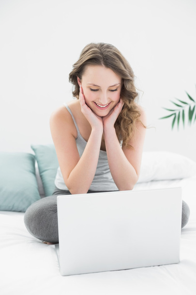 Smiling casual brunette looking at laptop in bed - Foto, imagen