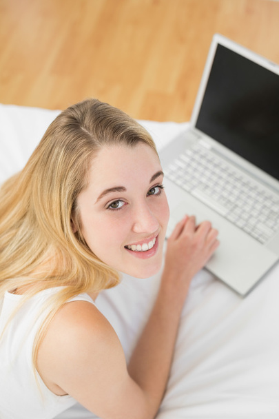 Peaceful blonde woman working with her notebook lying on her bed - Foto, Imagen