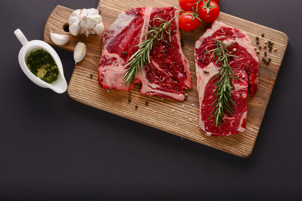 Fresh raw beef steak on wooden cutting board over black background with spices, top view. - Fotó, kép
