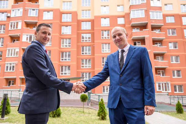 Dois homens de negócios apertando a mão antes do novo edifício ao ar livre
 - Foto, Imagem