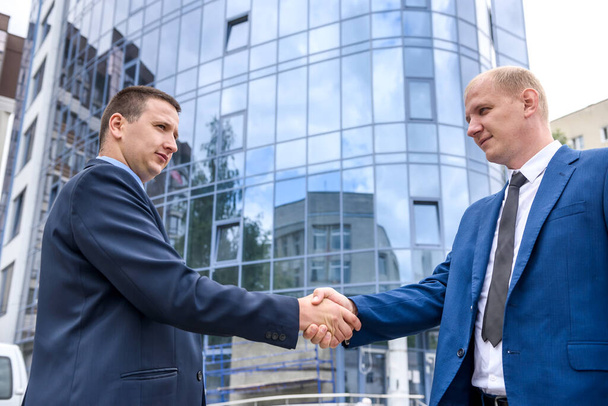 Twee zakenmannen die elkaar de hand schudden voor nieuwbouw buiten - Foto, afbeelding
