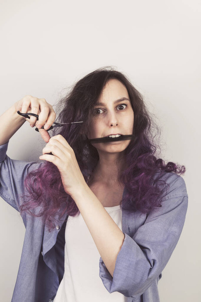 Young girl cuts to herself curly purple hair. Gray background. Toned - Fotografie, Obrázek