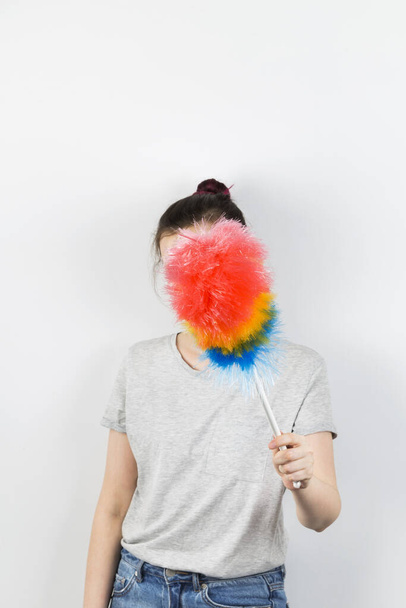 Girl holds brush to clean dust and closes her face on grey background - Foto, imagen