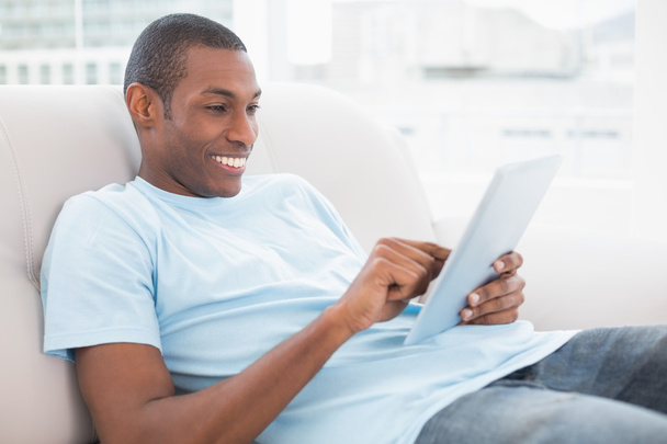 Casual smiling Afro man using digital tablet on sofa - Foto, Imagen