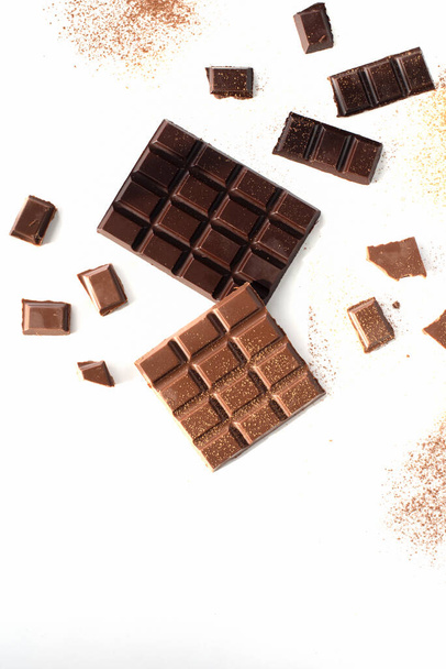 pieces of black and milk chocolate with cocoa powder are scattered on a white background - Fotoğraf, Görsel