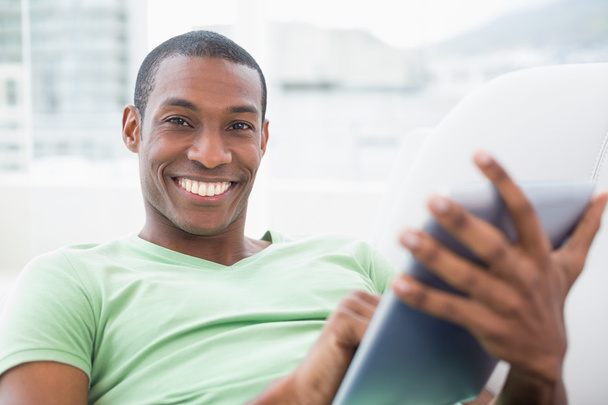 Casual smiling Afro man using digital tablet on sofa - Foto, imagen