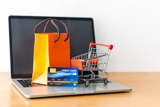 kredietkaart en kar supermarkt en oranje papieren zak op houten tafel. winkelconcept - Foto, afbeelding