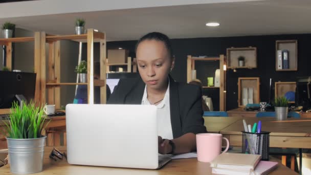 Young african american woman typing on laptop and drinking a coffee from a pink cup - Materiaali, video