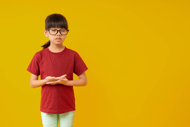 Portrait of Young Asian kid student standing and making meditation, cute Thai girl in red shirt with school bag making calm down and meditating for knowledge before learning - Photo, Image