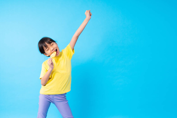 Jeune fille asiatique enfant manger de la crème glacée et poster drôle sur fond bleu en studio
 - Photo, image