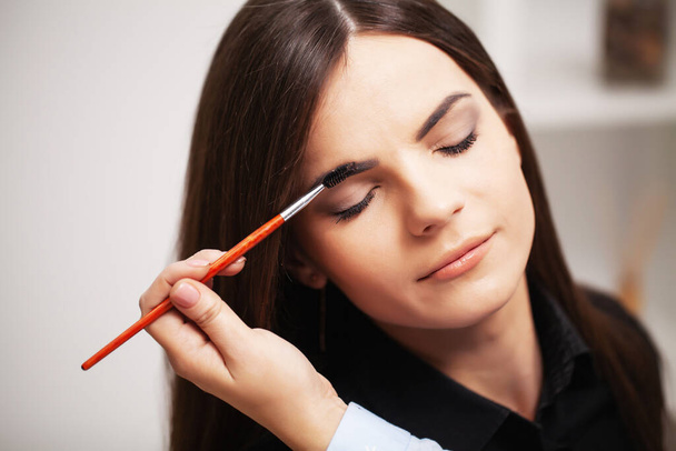 Mooi meisje maakt gebruik van de diensten van een professionele make-up kunstenaar in een beauty studio - Foto, afbeelding