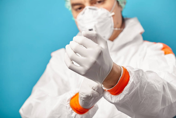 Male nurse put on sterile glove over plain blue background, close-up view. Environmental friendliness and safety during medical procedures. - 写真・画像
