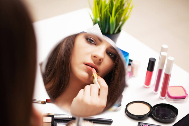 Menina bonita aplica maquiagem no rosto em casa perto do espelho
 - Foto, Imagem