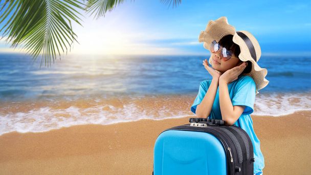 Młody, ładny azjatycki dzieciak z torbą podróżną w stylu letnim, tajska dziewczyna w kapeluszu z tłem morza i plaży na wakacjach  - Zdjęcie, obraz