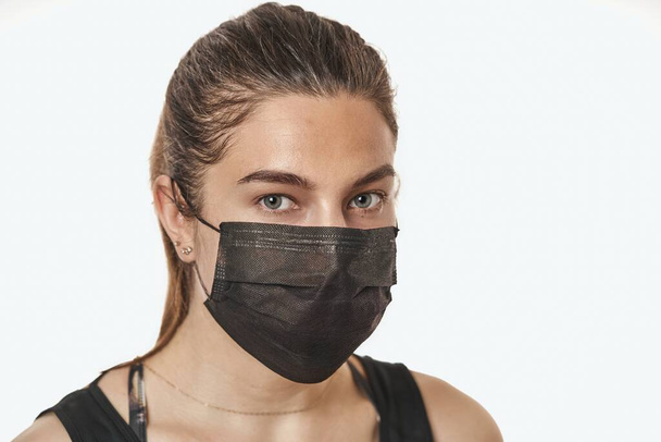 A close-up portrait of a pretty female wearing a surgical mask isolated on a white background - Foto, imagen