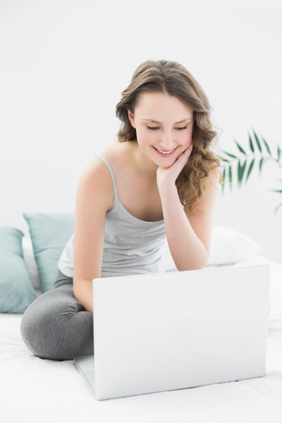Smiling casual brunette looking at laptop in bed - Photo, Image