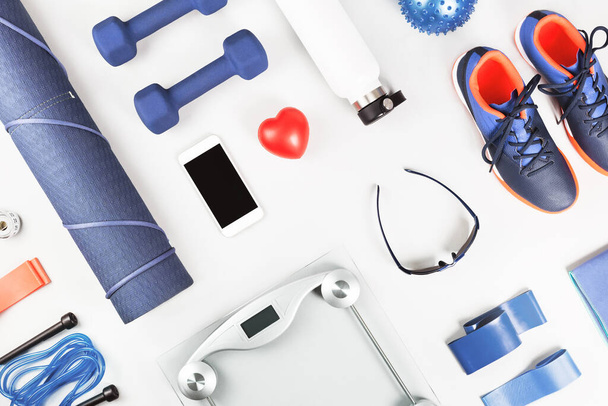 Healthy lifestyle blue and red gender neutral sports accessories knolling flat lay on light grey with heart and smartphone in the middle. Fitness excersise and weight management concept - Fotoğraf, Görsel