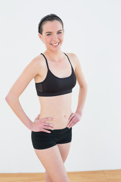 Smiling toned woman with hands on hips in fitness studio - Photo, image