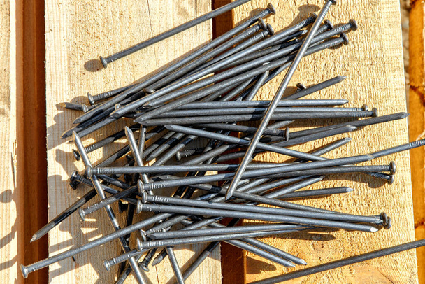 Iron nails on a wooden background. Long, metal, carpenter's nails lie on the lumber for construction. Top view. Flatlay. - Foto, Imagem