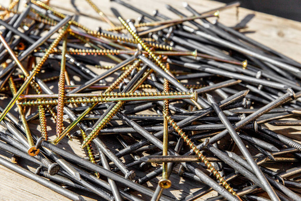 Iron nails and screws on a wooden background. Long, metal, carpenter's nails and self-tapping screws for construction. Fixing tool. The view from the top - Photo, Image