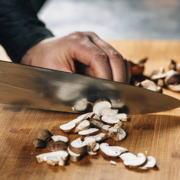Chef cutting shiitake mushrooms with knife on a wooden cutting board - Foto, afbeelding