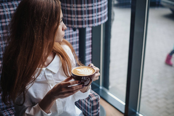 Woman holding coffee mug looking in the window - Фото, изображение