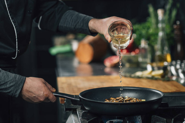 Chef pouring white wine into a frying pan with sliced shiitake mushrooms - Foto, immagini