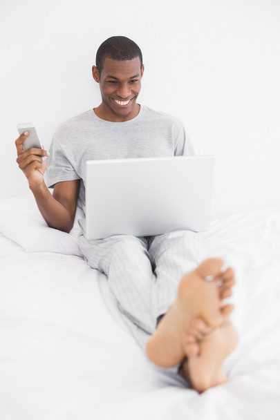 Afro man text messaging while using laptop in bed - Fotoğraf, Görsel