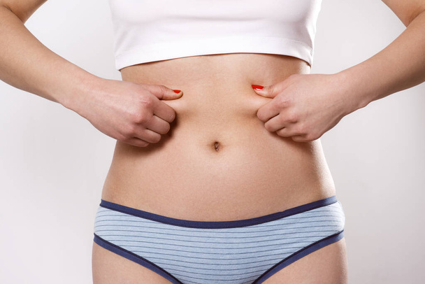 the woman pinches the excess fat on her sides and belly with her fingers. On a white background, close-up - Фото, изображение
