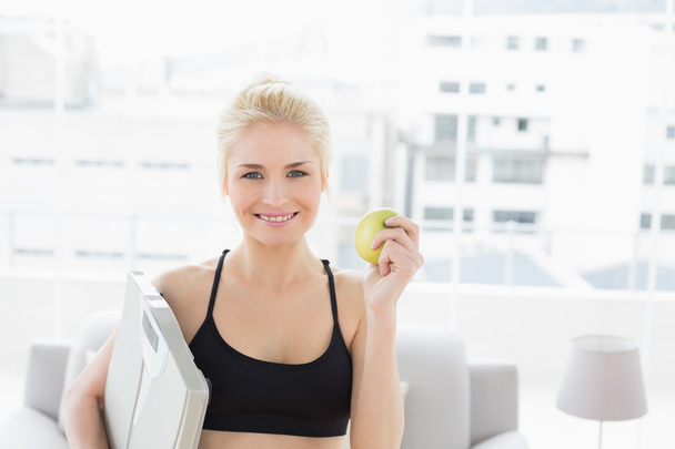 Smiling fit woman holding scale and apple in fitness studio - Foto, Imagem