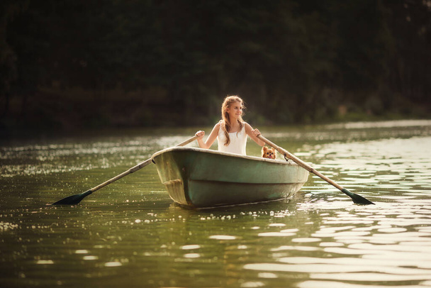 Young girl with a small dog in a boat on the lake in the rays of light - Foto, imagen