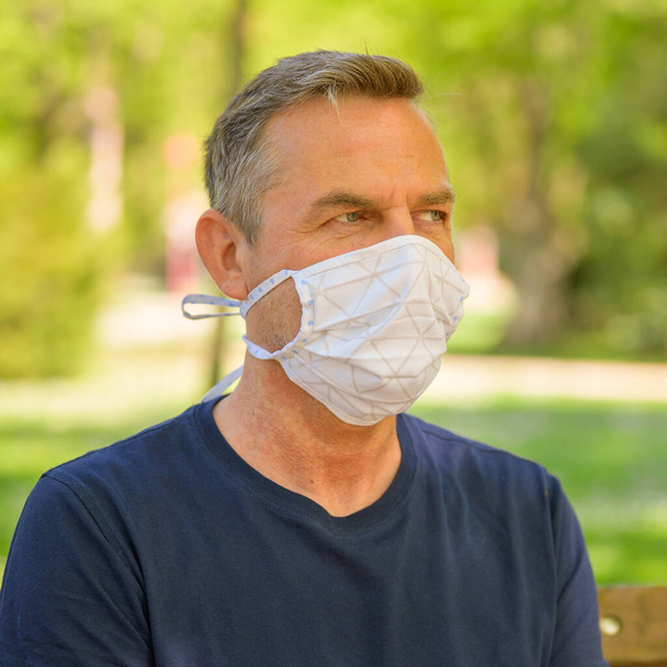 Mann mittleren Alters entspannt sich mit einer Gesichtsmaske als Infektionskontrolle gegen das Atemwegsvirus während der Coronavirus oder Covid-19-Pandemie im Freien in einem Park mit Kopierraum - Foto, Bild
