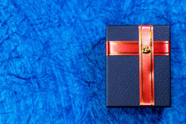 Ένα μπλε κουτί δώρου με κόκκινη κορδέλα και ένα αυτοκόλλητο καρδιάς πάνω του. Έννοια δώρων γάμου - Φωτογραφία, εικόνα