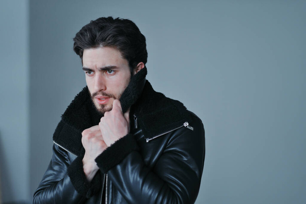 A large portrait of a stylish young man with a beard and dark hair in a black leather jacket - Foto, Imagen