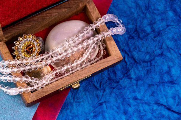 Close up shot of shining glass and amber jewellery in a wood case with velvet cloth over blue background - Photo, Image