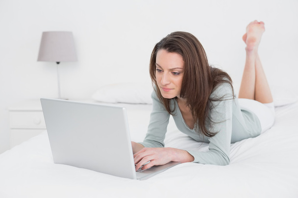 Relaxed casual woman using laptop in bed - 写真・画像