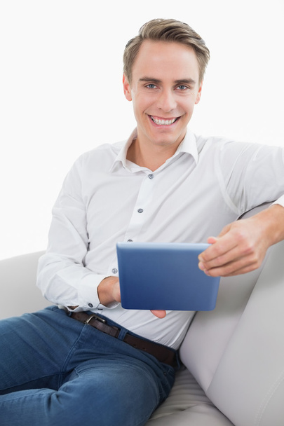 Casual smiling young man using digital tablet on sofa - Valokuva, kuva