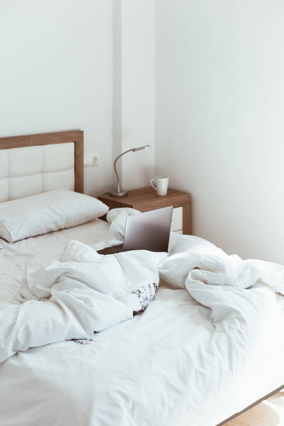 Working home quarantine self isolation lockdown concept. Laptop in unmade bed. Comfortable and cozy remote home office. Modern apartments with sunlight and minimalistic design. Stay safe in pandemic. - Foto, Imagem