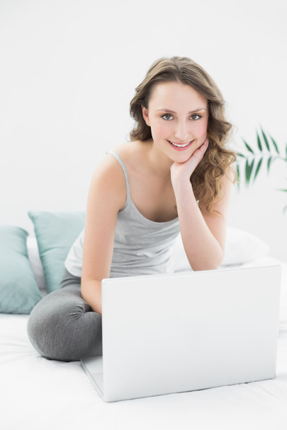 Smiling casual brunette with laptop sitting in bed - Fotoğraf, Görsel