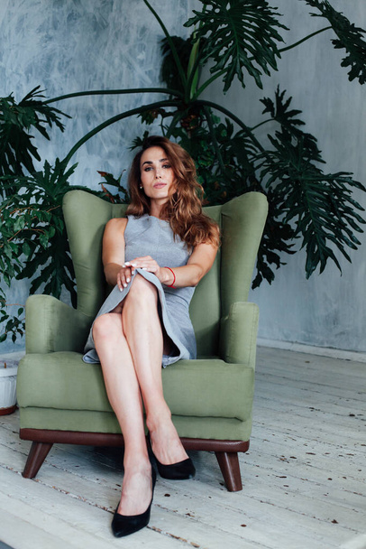 Portrait of a beautiful fashionable woman in a gray dress sitting in a green chair - Foto, afbeelding