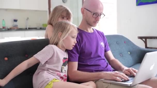 Soggiorno a casa padre seduto divano utilizzando il computer con due bambini di sesso femminile bambino lavoro a distanza, insieme, concetto di svago
 - Filmati, video