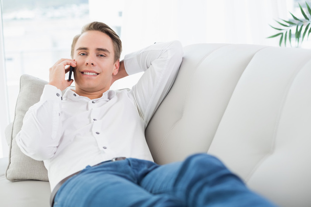Relaxed young man using cellphone while lying on sofa - Фото, зображення