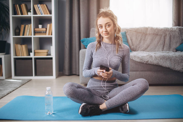 Женщина сидит на коврике для йоги со смартфоном и наушниками
 - Фото, изображение
