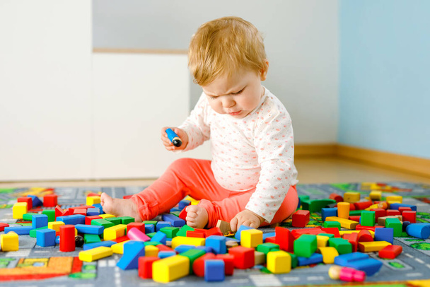 教育用のおもちゃで遊んでいる愛らしい赤ちゃんの女の子。国内の部屋でカラフルな異なる木製のブロックで楽しい時間を過ごしている幸せな健康な子供。赤ちゃんの学習の色と形 - 写真・画像