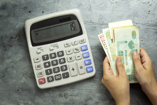 zbliżenie ręce trzymając algierskiej waluty urzędowej (dinar algierski) i przy użyciu dużego szarego kalkulatora do liczenia  - Zdjęcie, obraz