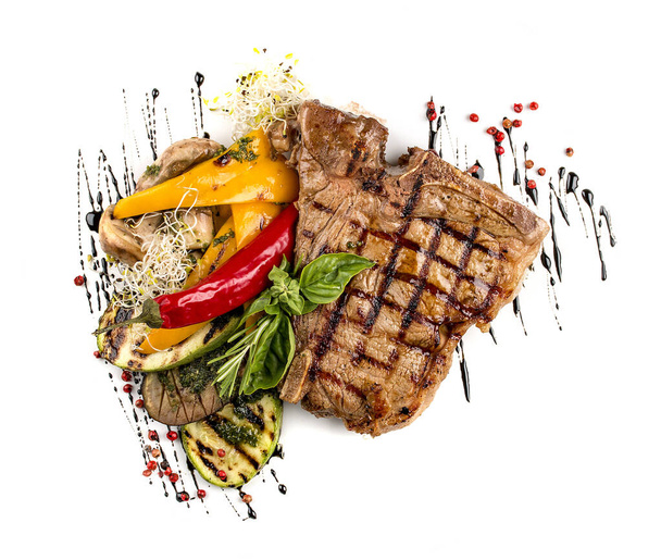 Tender grilled steak or T-bone steak served with grilled vegetables on a white plate. - Photo, Image