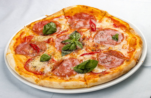Pyszna gorąca pizza z salami, serem, pomidorami i różnymi przyprawami. Na białym tle - Zdjęcie, obraz
