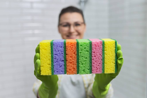 House cleaning concept. Woman in protective gloves holding many cleaning sponges, background bathroom interior, white ceramic tile - Foto, Imagen