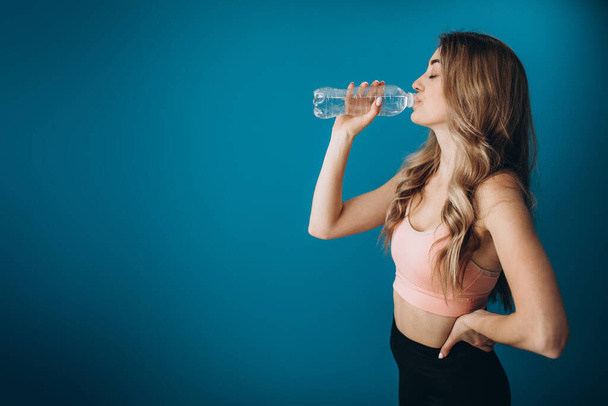 Δυνατό κορίτσι πίνοντας φρέσκο νερό πάνω από το μπλε στούντιο φόντο - Φωτογραφία, εικόνα