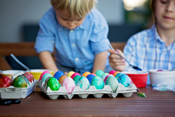Sweet children, brothers, coloring and paiting eggs for Easter in garden, outdoors at home in backyard - Foto, afbeelding